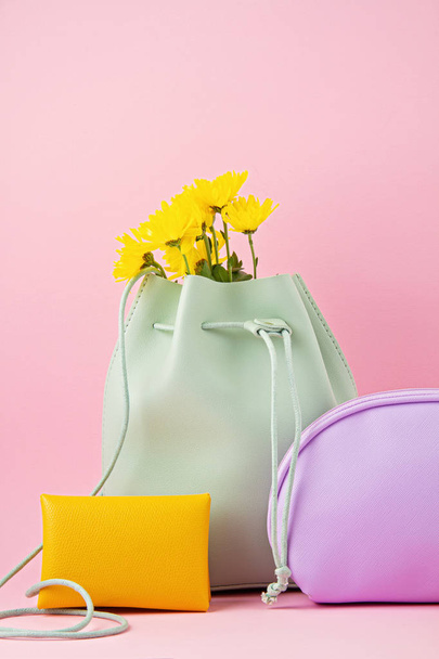 Lányok bőr kiegészítők fényes pasztell színek: kéz rossz, pénztárca, make-up táska és virágok felett rózsaszín háttér.  - Fotó, kép