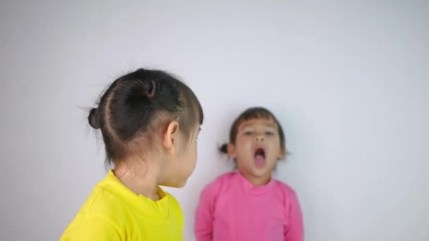 Retrato de una niña asiática feliz sonriente y su hermana mayor malhumorada detrás aislada sobre fondo blanco
. - Imágenes, Vídeo