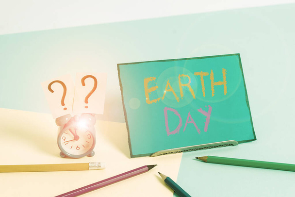 Writing note showing Earth Day. Business photo showcasing Worldwide celebration of ecology environment preservation Mini size alarm clock beside stationary on pastel backdrop. - 写真・画像
