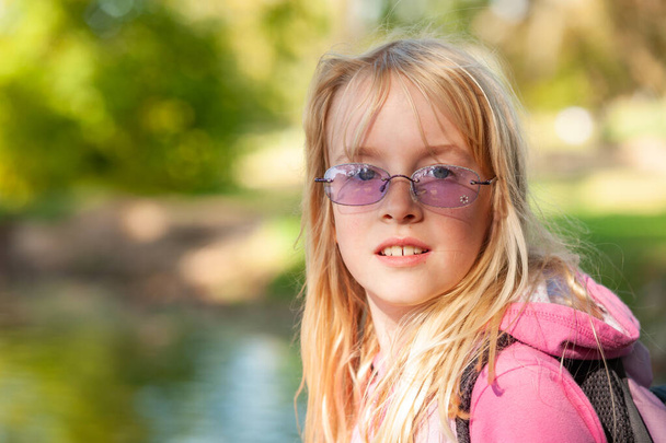 Красивая молодая блондинка в фиолетовых солнцезащитных очках с расплывчатой зеленой листвы на заднем плане
 - Фото, изображение