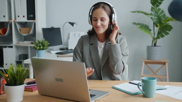 Playful lady listening to music in headphones dancing working with laptop having fun - Séquence, vidéo
