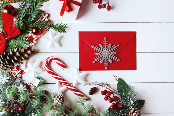 Χριστουγεννιάτικη σύνθεση. Χριστουγεννιάτικο δώρο, κουκουνάρια, κλαδιά ελάτης σε ξύλινο λευκό φόντο. Κενή χριστουγεννιάτικη κάρτα με φάκελο επίπεδη lay, πάνω όψη, αντίγραφο χώρου. Νέο έτος. - Φωτογραφία, εικόνα