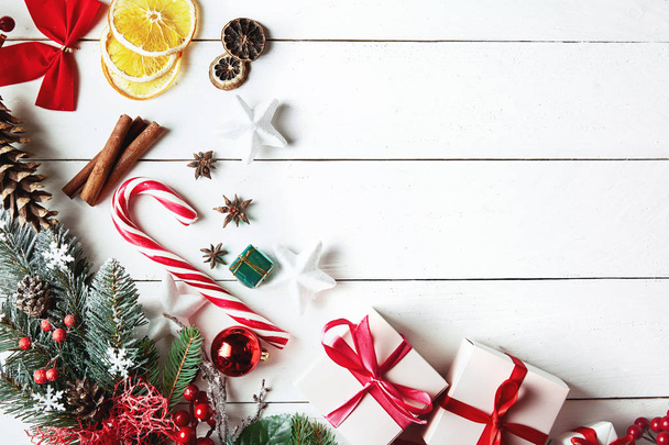 Krásné vánoční kompozice na bílém pozadí s vánoční dárkové krabice, zasněžené jedlové větve, jehličnany, vánoční dekorace, sušené ovoce, karamelové tyčinky a červené bobule. Horní pohled - Fotografie, Obrázek