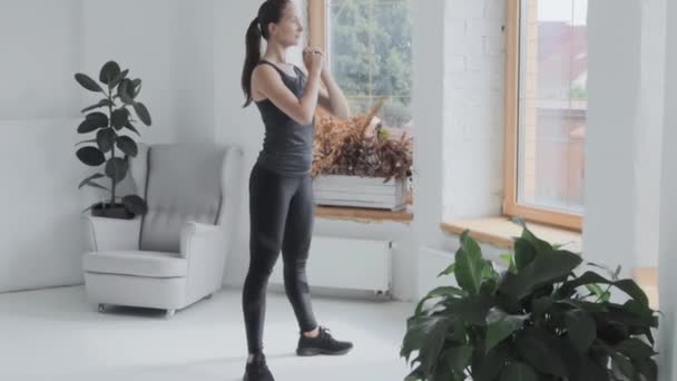 Giovane ragazza bruna in abbigliamento sportivo fa esercizi sportivi a casa. Facendo squat
 - Filmati, video