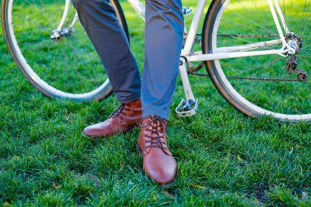 Κοντινή φωτογραφία του mans δερμάτινες μπότες σε πράσινο γρασίδι andretro ποδήλατο  - Φωτογραφία, εικόνα