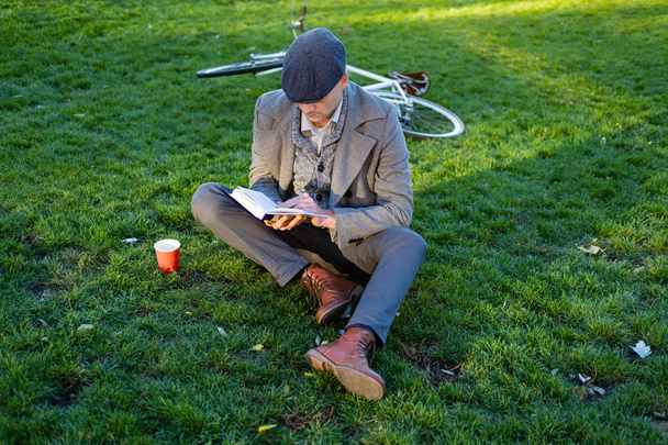 Junge männliche Hipster mit Retro-Fahrrad lesen Buch im Herbstpark - Foto, Bild