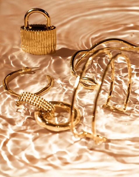 Bracelets dorés, boucles d'oreilles, bagues, bijoux sur l'eau dorée backgr
 - Photo, image