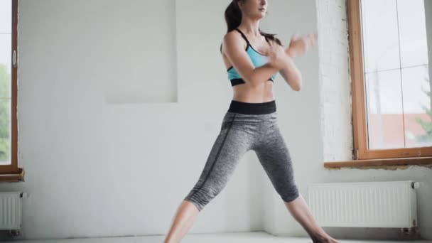 Νεαρή σπορ μελαχρινή κοπέλα στα αθλητικά κάνει ασκήσεις στο φωτεινό δωμάτιο στο σπίτι - Πλάνα, βίντεο