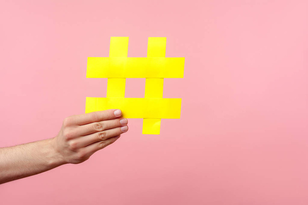 Closeup of male hand holding large yellow hashtag sign, concept of marketing and promotion in internet, followers in social media, trend content. indoor studio shot isolated on pink background - Фото, зображення