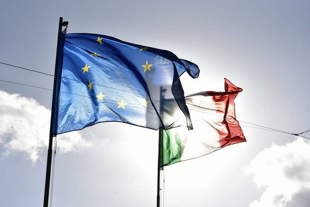 Avrupa bayrağı ve İtalyan bayrağı açık mavi gökyüzünde birlikte dalgalanıyor. Avrupa Birliği ile İtalya arasındaki ilişki hakkında. Kavramlar. - Fotoğraf, Görsel