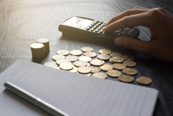 Κοντινό χέρι του ανθρώπου χρησιμοποιώντας αριθμομηχανή με χρυσά νομίσματα, στυλό, σημειωματάριο σε μαύρο τραπέζι. Επιχειρήσεις, χρηματοοικονομικά, μάρκετινγκ, έννοια και σχεδιασμός ηλεκτρονικού εμπορίου - Φωτογραφία, εικόνα