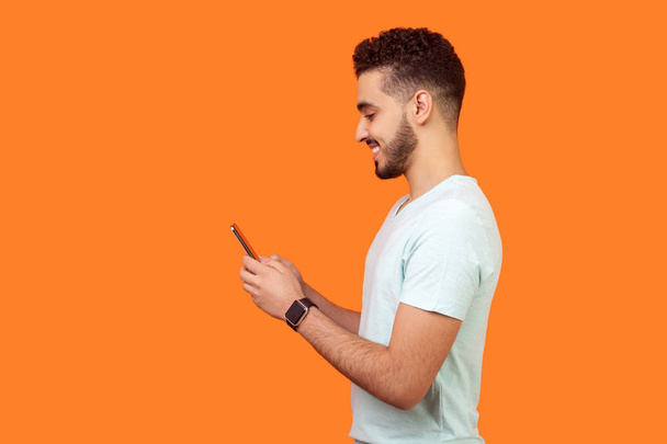 Side view of happy brunette man smiling while using cellphone. e - Foto, immagini