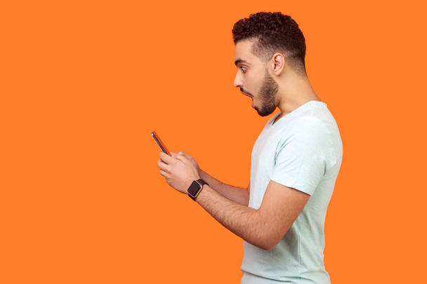 Side view of amazed brunette man looking shocked at mobile phone - Foto, immagini
