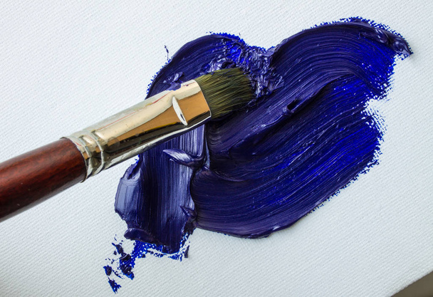 Spot of blue oil paint and art brush on white canvas - Фото, изображение