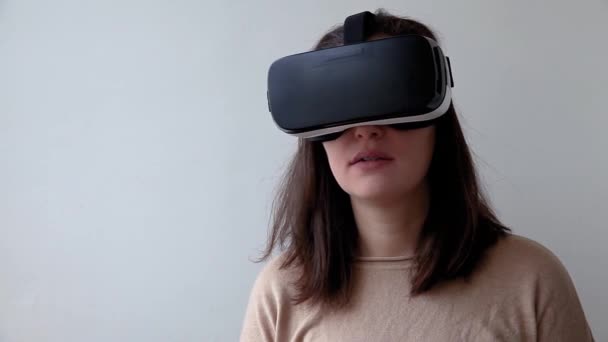 Sonríe mujer joven usando realidad virtual gafas VR casco auriculares sobre fondo blanco. Smartphone con gafas de realidad virtual. Tecnología, simulación, alta tecnología, concepto de videojuego. - Metraje, vídeo