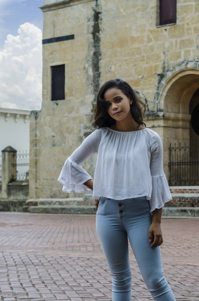 Außenporträt eines jungen schönen Mädchens von 9 bis 25 Jahren, das auf der Straße posiert. trägt weiße Bluse und enge Jeans und Sapatillas. Lebensstil in der Stadt. weibliches Modekonzept. - Foto, Bild
