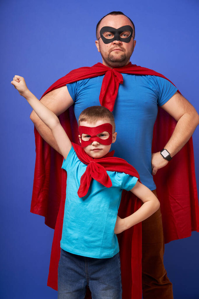 Dad and son superheroes in red cloaks on blank blue background - Фото, зображення