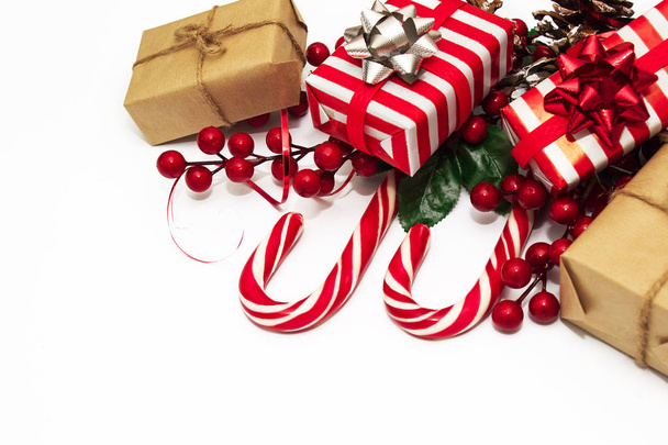 Décor de Noël. Carte de Noël avec une branche aux baies rouges et cônes, ornée d'un ruban rouge. Coffrets cadeaux en papier à rayures rouges et blanches. Bonbons de Noël. Pose plate et espace de copie
. - Photo, image