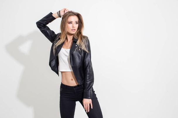 A girl in a leather jacket and black pants posing on a white background. Fashion shooting - Photo, image