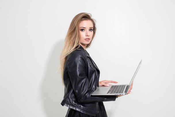 A girl in a black leather jacket with a laptop posing on a white background. Fashion shooting - Fotografie, Obrázek