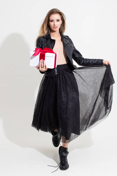 Chica sosteniendo un regalo en una caja blanca con una cinta roja y posando sobre un fondo blanco
 - Foto, Imagen