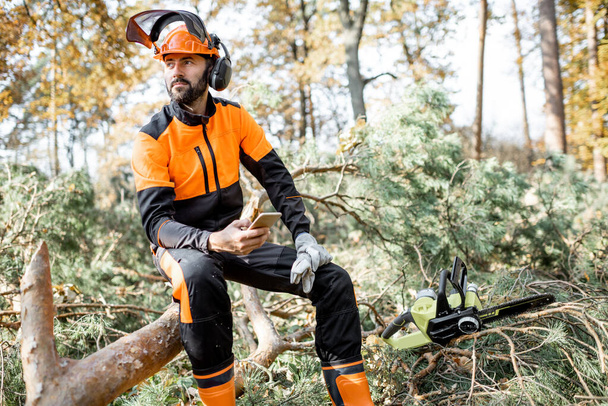 Professional lumberman resting with phone in the forest - 写真・画像