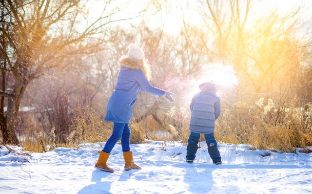 Children play in a snowy winter park at sunset. Throw snow and have fun. Winter fun. Holidays. - Photo, Image