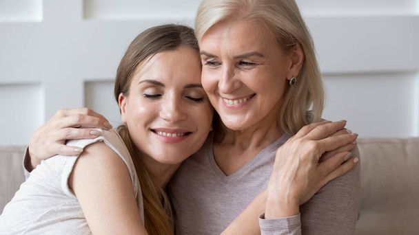 Peaceful smiling older retired mother embracing calm happy daughter. - 写真・画像