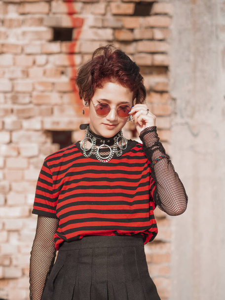Menina emo em um fundo de tijolo tira óculos redondos hipster. Corpos cortados
 - Foto, Imagem