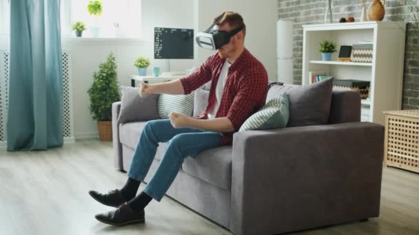 Carefree student wearing virtual reality glasses enjoying driving game at home - Video, Çekim