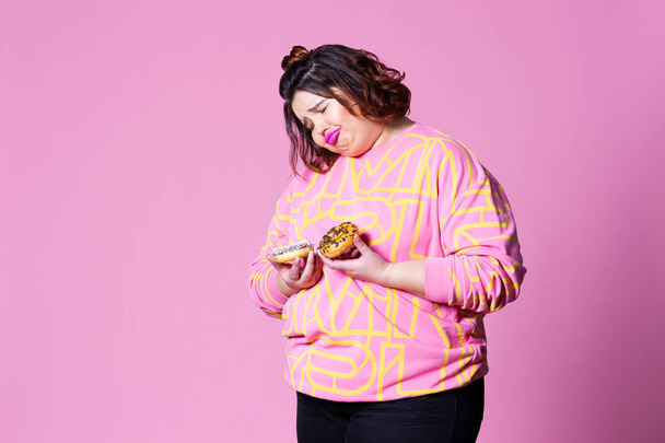 Sad plus size model with doughnuts, fat woman sadness and overeats on pink background - Фото, изображение