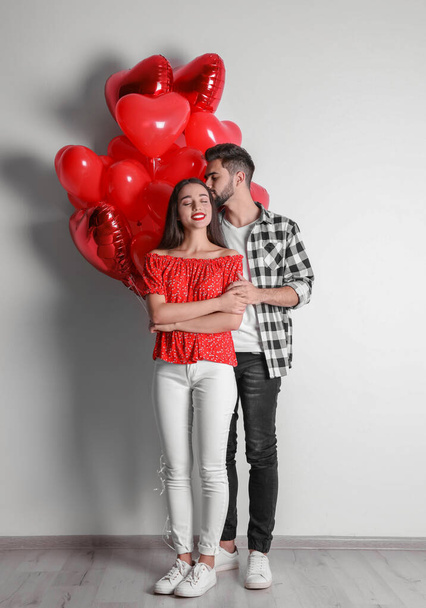 Happy young couple with heart shaped balloons near light wall. Valentine's day celebration - Zdjęcie, obraz
