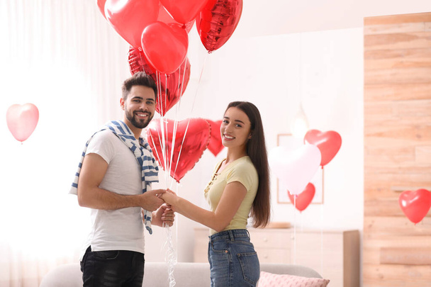 Happy young couple with heart shaped balloons in living room. Valentine's day celebration - Foto, Imagem