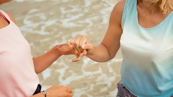 Mãe e filha adulta dão as mãos na costa do mar
 - Foto, Imagem