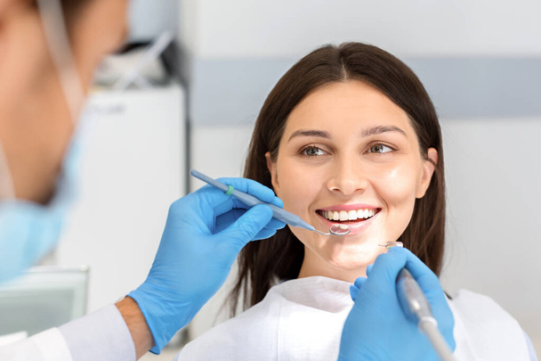 Lächelnde Frau blickt während der Behandlung vertrauensvoll zum Zahnarzt - Foto, Bild
