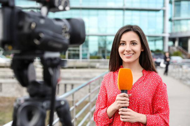 Young female journalist with microphone working on city street - Zdjęcie, obraz