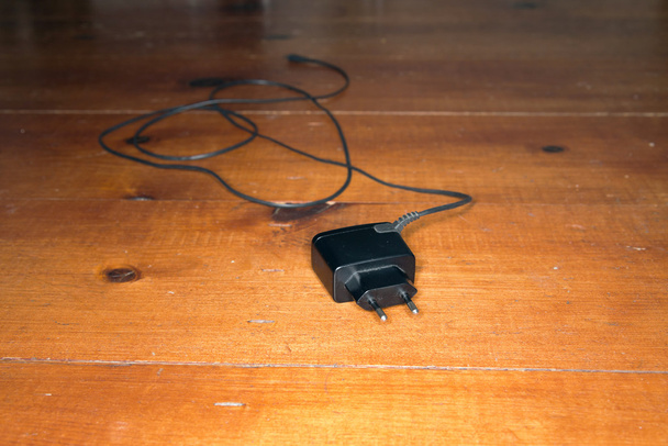 Cargador de batería electrónico negro para teléfono móvil en floo de madera
 - Foto, imagen
