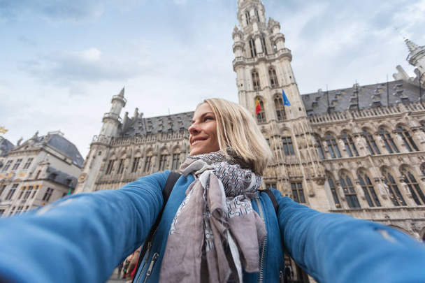 A woman takes a telephone picture on the background of the city hall in the main square Grand place in Brussels, Belgium - Photo, Image