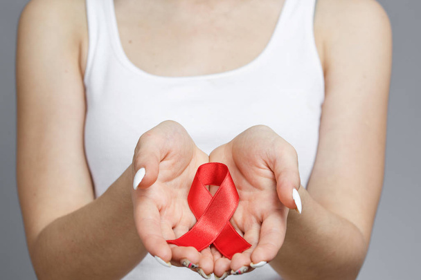 Руки женщины держат красную ленту для информирования о СПИДе
 - Фото, изображение