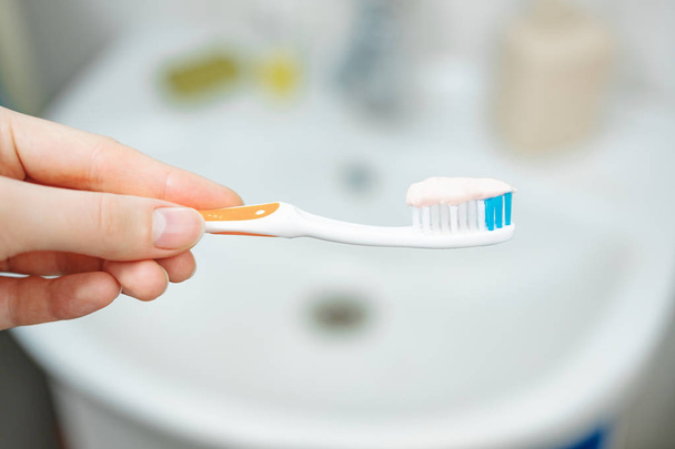 Hand holds a toothbrush with toothpaste on bathroom background, close up view.  - Photo, image