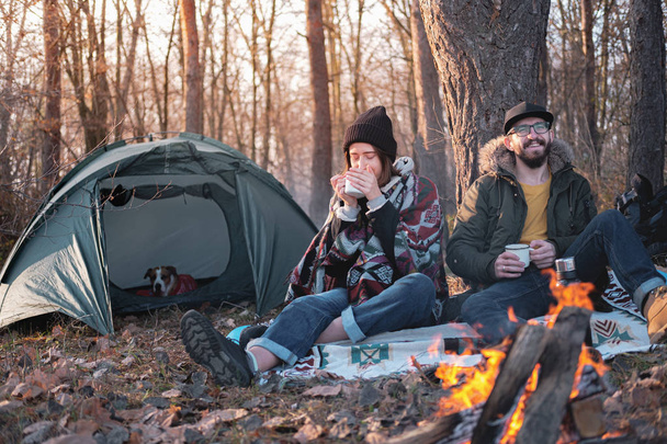 Two persons enjoying hot drinks by the bonfire at a camping site. - Foto, Imagem