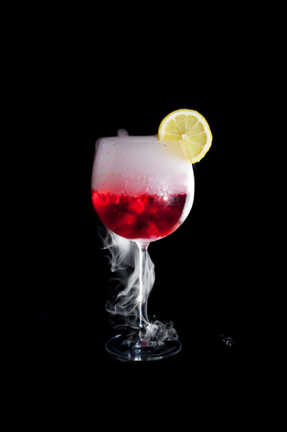 A cup of red cold cocktail with dry ice smoke and a lemon slice - Photo, Image