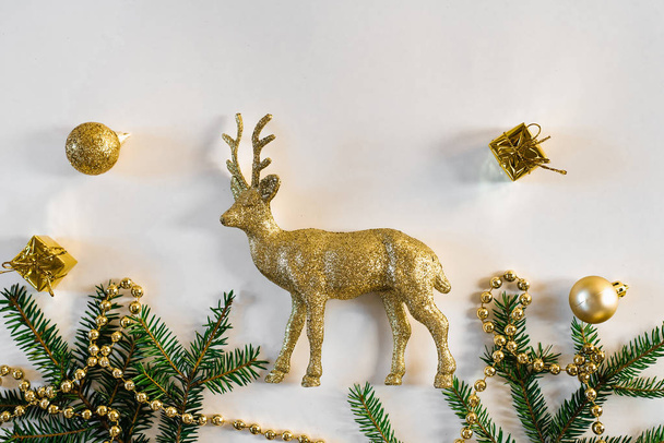 Noel ve yeni yıl kartı. Altın geyik ve Noel ağacı ladin dalları ile altın oyuncaklar, beyaz arka planda altın boncuklar - Fotoğraf, Görsel