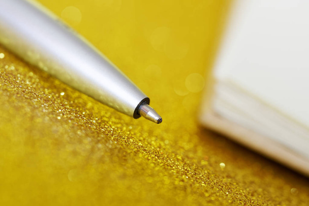 Uma caneta-tinteiro de prata encontra-se sobre um fundo dourado ao lado de uma nota
 - Foto, Imagem