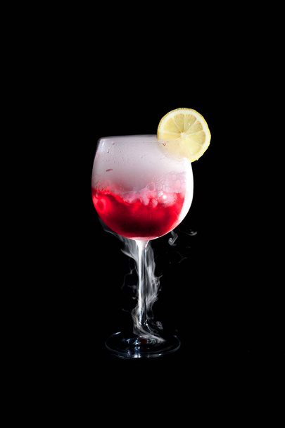 Une tasse de cocktail rouge froid avec de la fumée de glace sèche et une tranche de citron
 - Photo, image