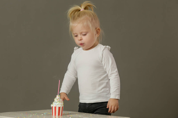 Studio laukaus lapsi tyttö puhaltaa syntymäpäivä kynttilän cupcake
 - Valokuva, kuva
