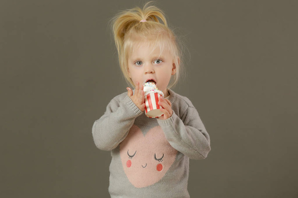 Studio shot of a toddler eating cupcakes with a whipped cream - Photo, Image
