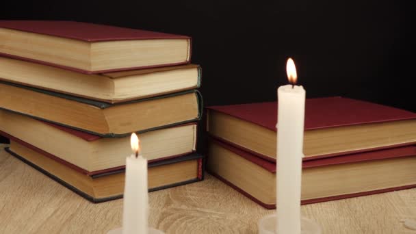 τα βιβλία τοποθετούνται το ένα πάνω στο άλλο υπό το φως των κεριών - Πλάνα, βίντεο