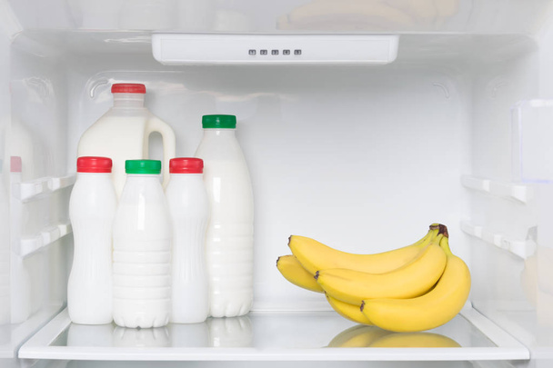 yogurts and bottled milk on a shelf in the refrigerator with bananas, light breakfast - Foto, immagini