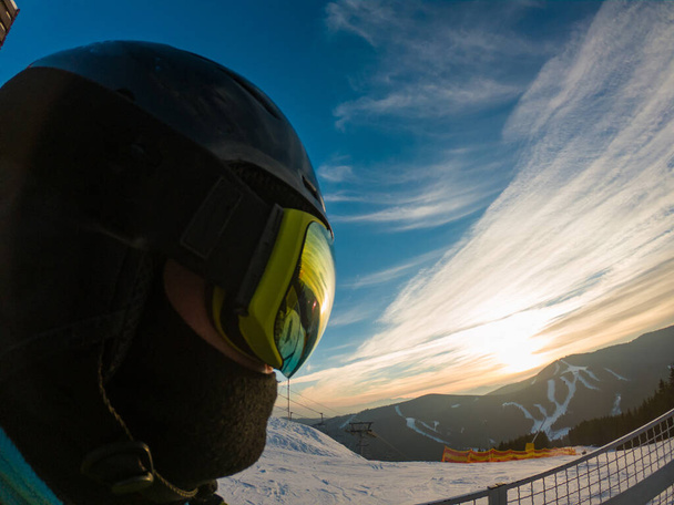 Ένας άντρας με μάσκα του σκι από κοντά. αντανάκλαση. Χιονισμένα βουνά στο ηλιοβασίλεμα - Φωτογραφία, εικόνα